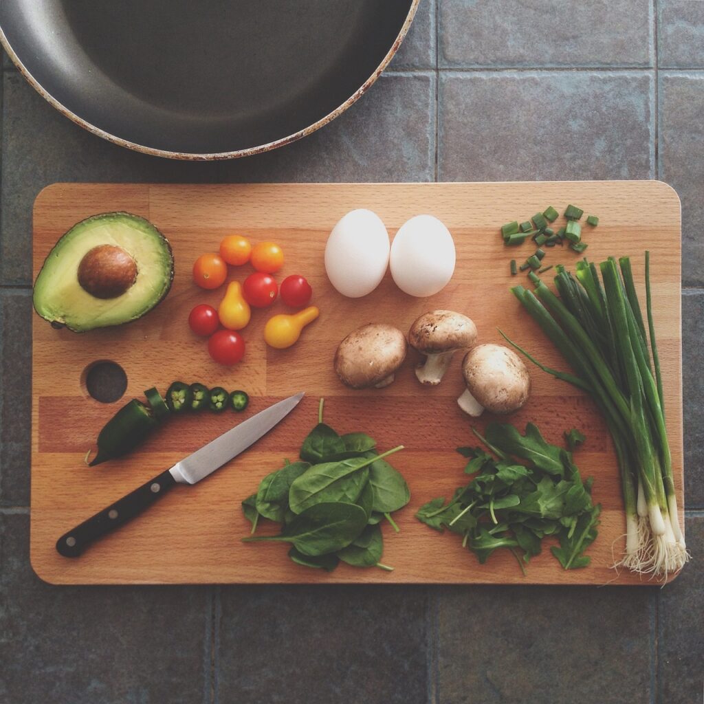 Planche à découper avec un avocat, des herbes aromatiques, des oignons nouveaux, des oeufs, des champignons, des tomates cerises