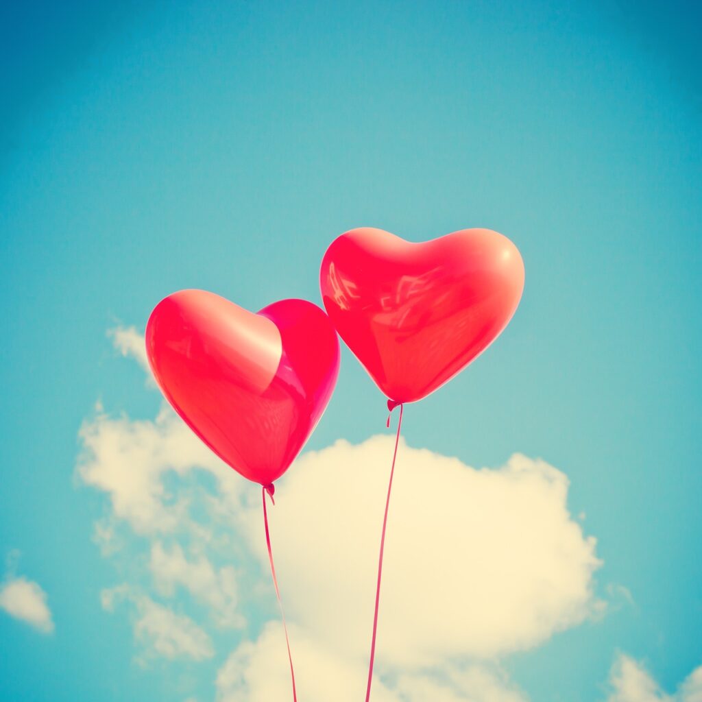 Deux ballons en forme de coeur volent dans le ciel, l'un à côté de l'autre à l'image d'un couple