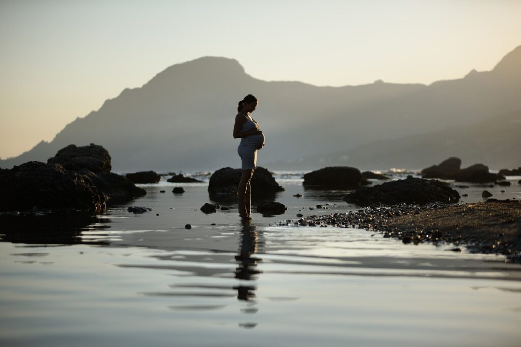 Femme enceinte debout sur une plage les pieds dans l'eau