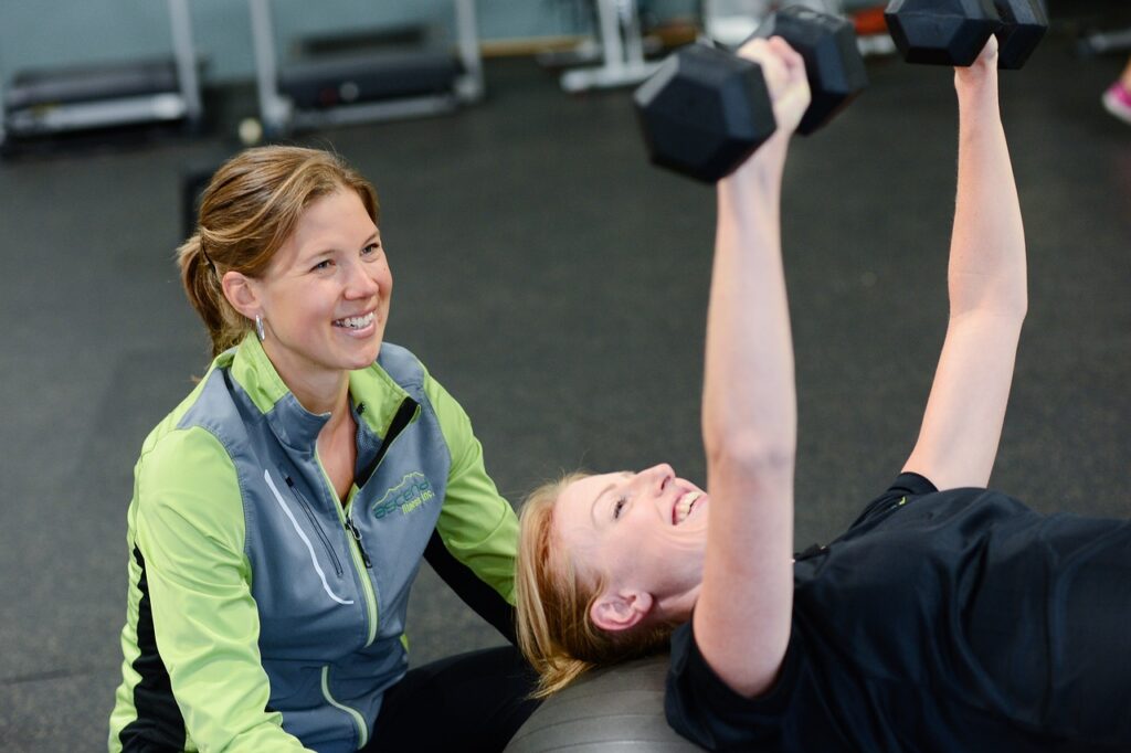 Femme couché sur un banc qui fait du chest press, coachée par une autre femme sportive